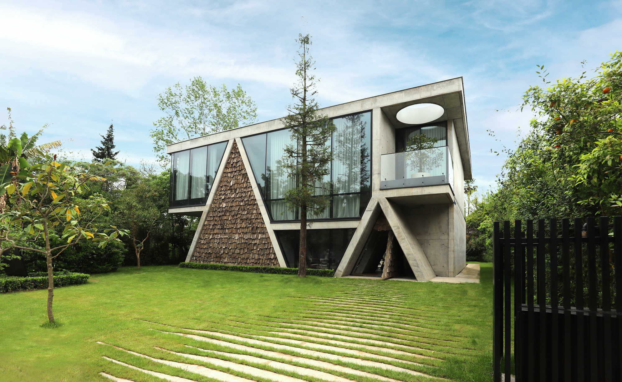 Exterior view of Gable Villa in Royan, Iran, showing its distinctive gabled roof and concrete materiality, set within a natural landscape.
