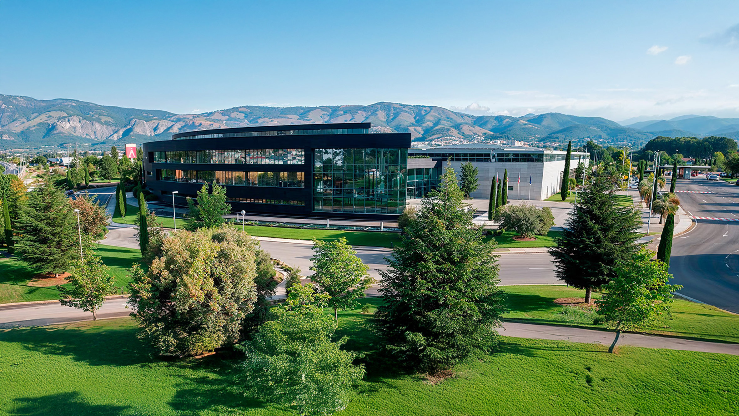 Exterior view of Actiu Technology Park showing modern industrial buildings integrated with extensive native Mediterranean landscaping under a clear sky.