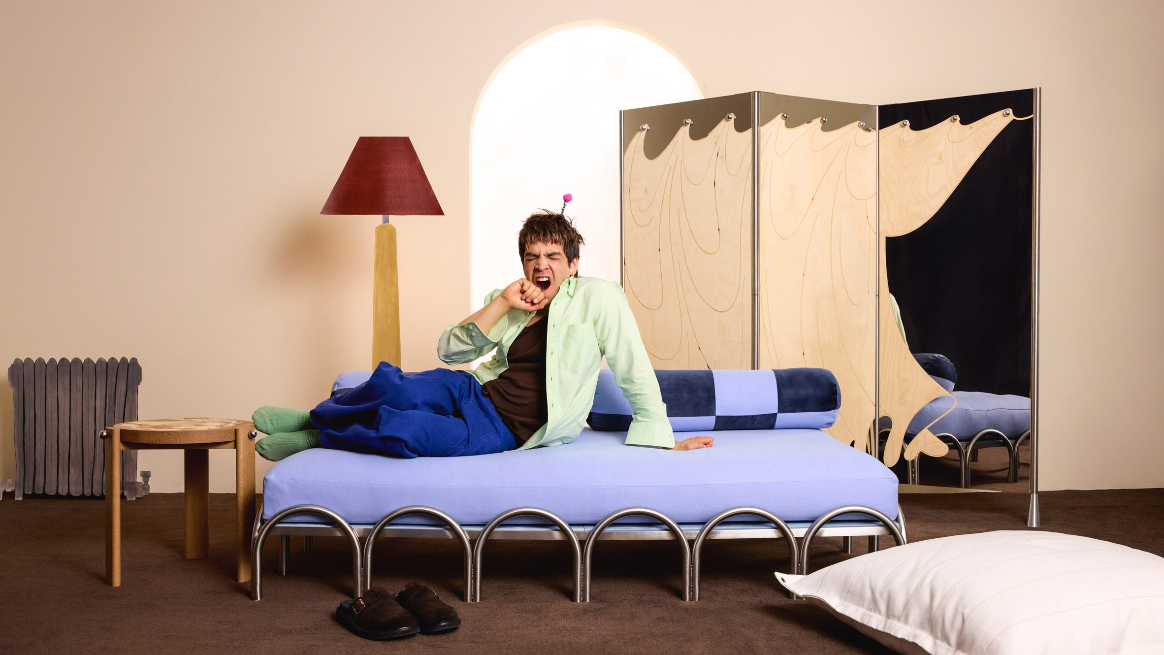Landing Daybed from the All Other Passports collection by Julio Torres and Sabai, featuring a stainless-steel arched base and light blue upholstery.