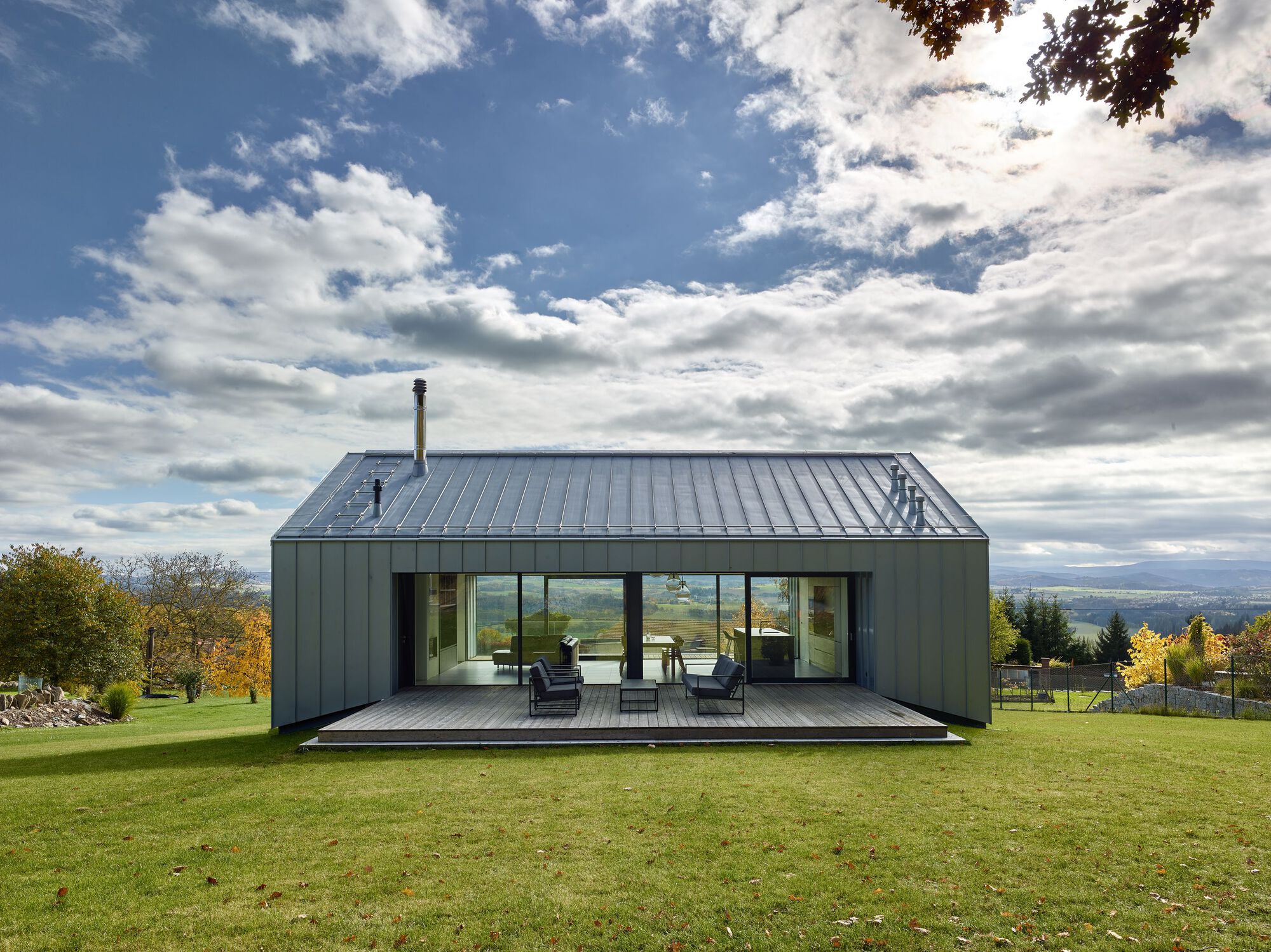 Exterior view of a modern house integrated into a sloping landscape, overlooking a mountain horizon.