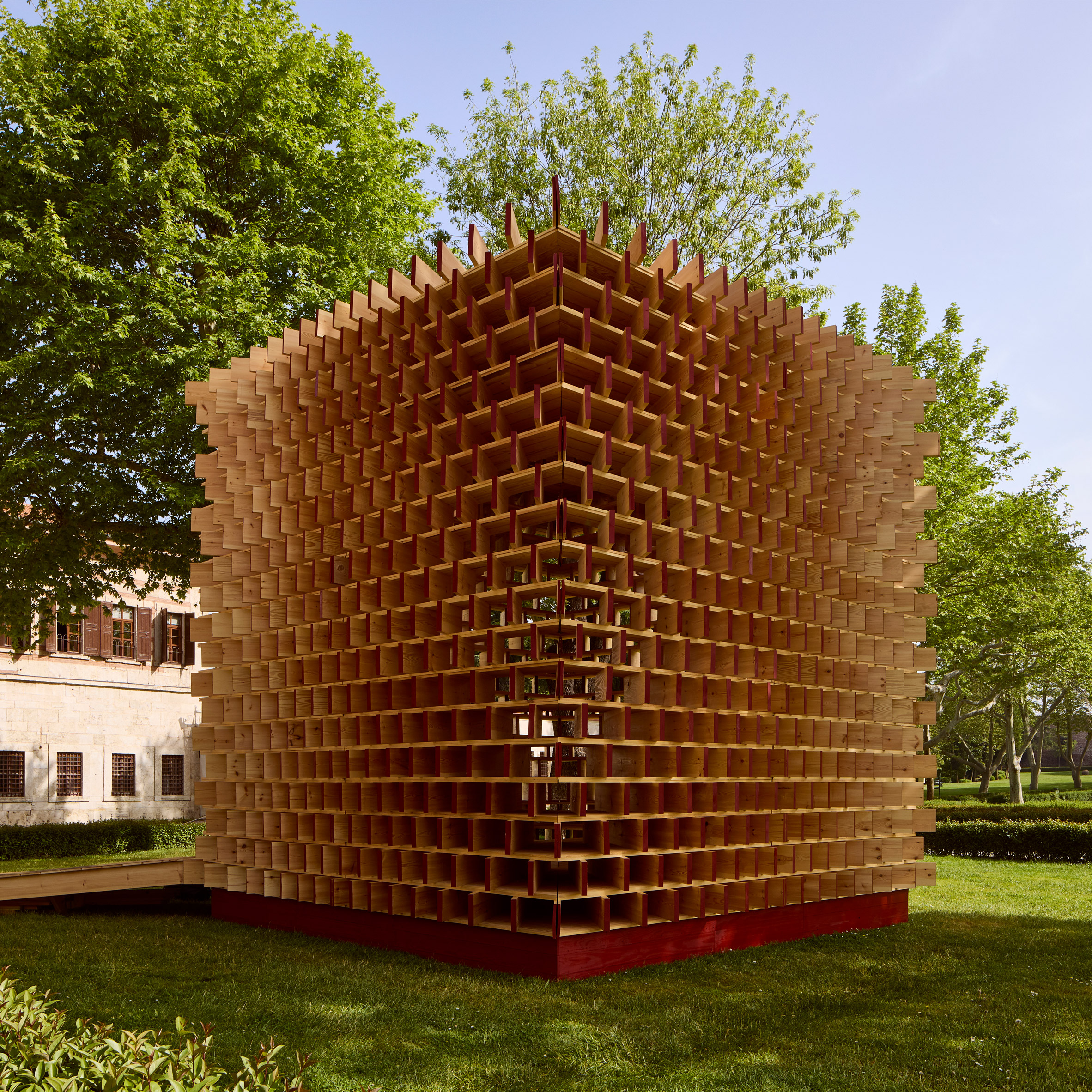 Exterior view of Waugh Thistleton Architects' "Pavilion of the Moment," a cuboid timber structure with vertical pine planks, set against the historic Hagia Irene church in