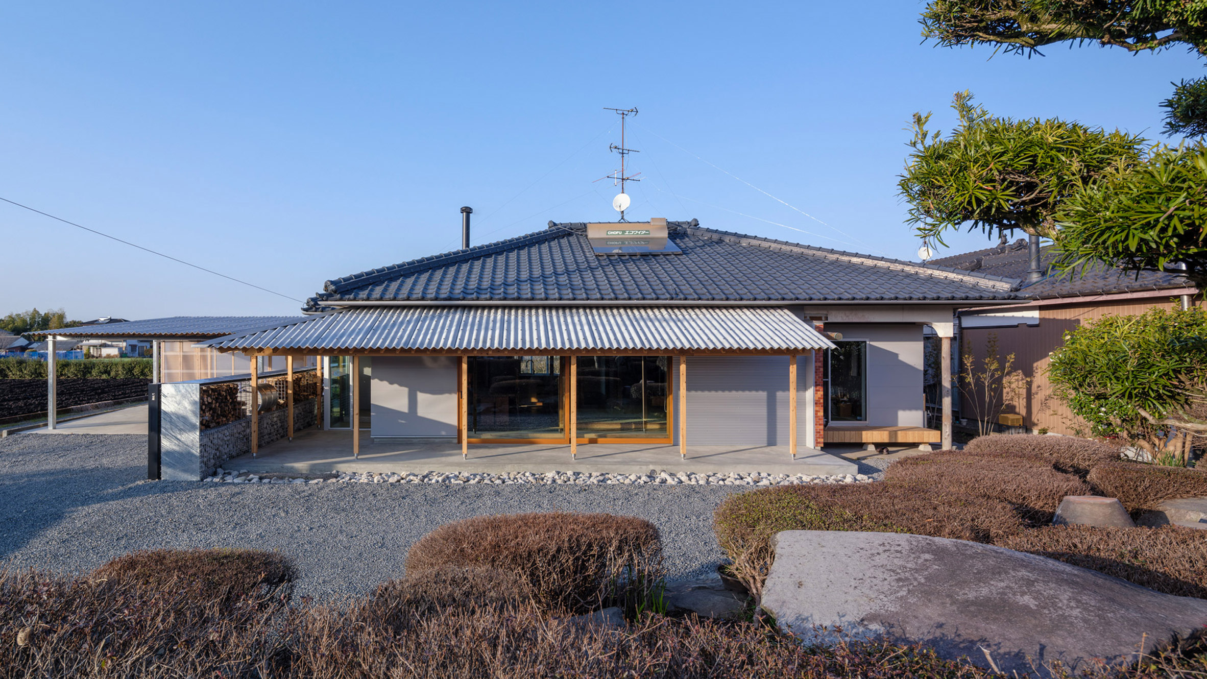 Exterior view of the renovated House in Miyakonojo by YNAS, showing timber-framed canopies extending from the eaves, providing shade over an outdoor living space.