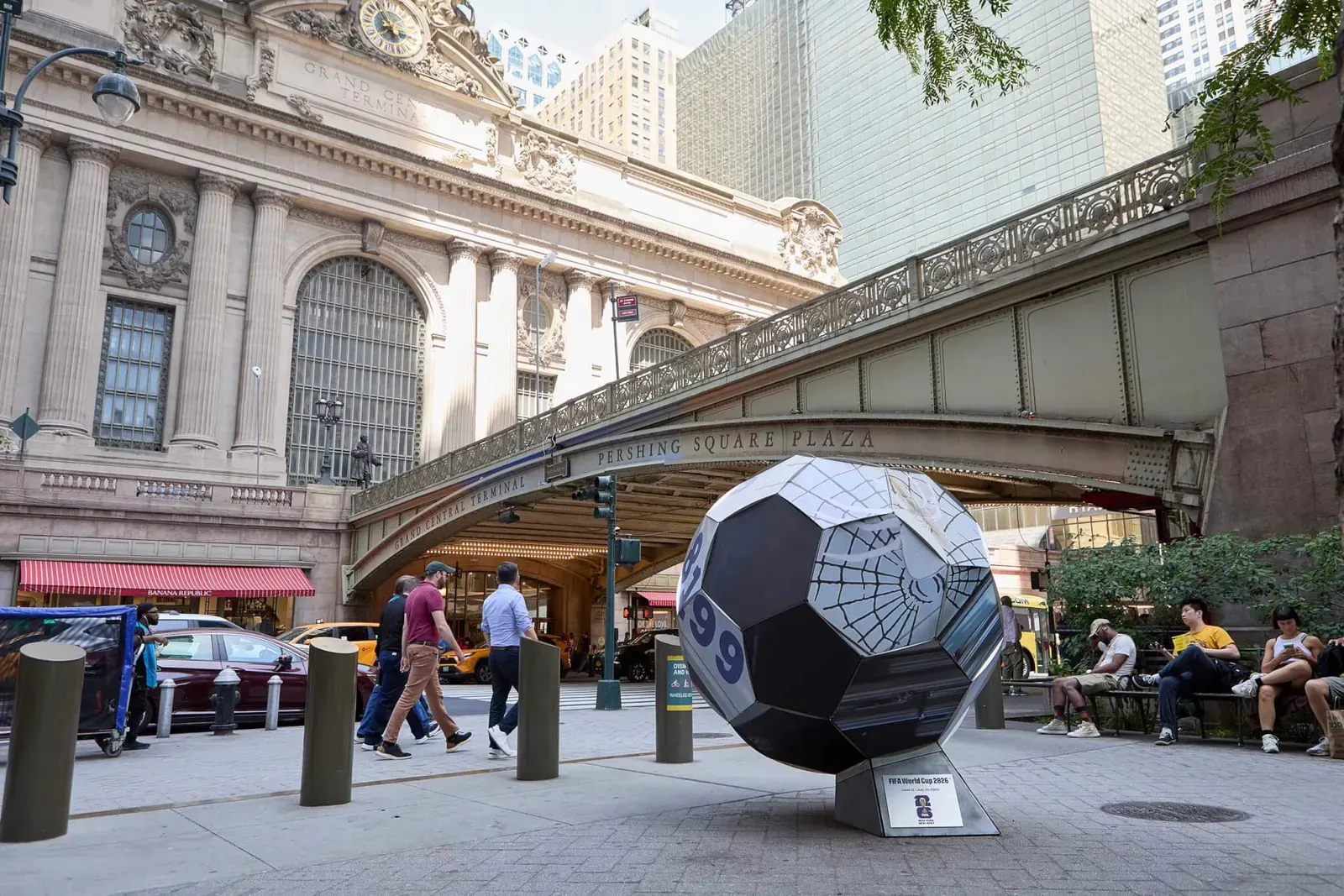 A large, artistically decorated soccer ball sculpture prominently displayed in a public urban setting.