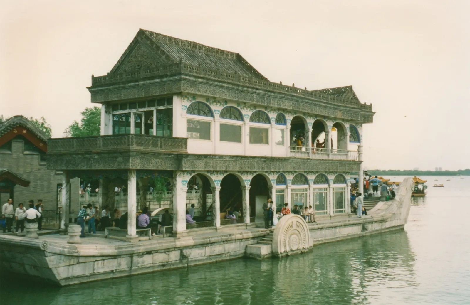 A contemporary red-painted wooden pavilion situated beside a lake, with a clear sky above.