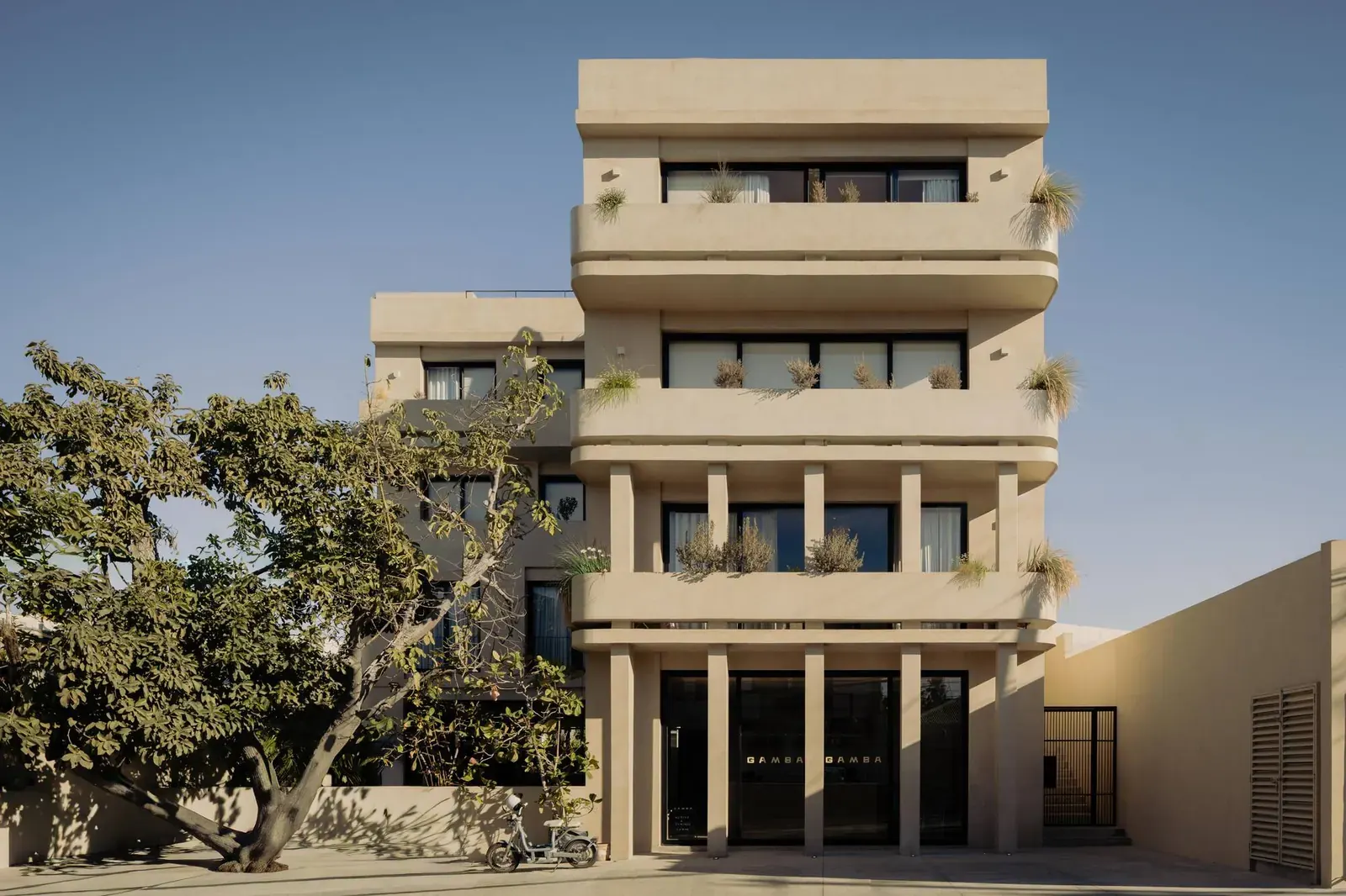 Exterior view of the Estero Residences and Gamba Café featuring a facade with balconies and plants.