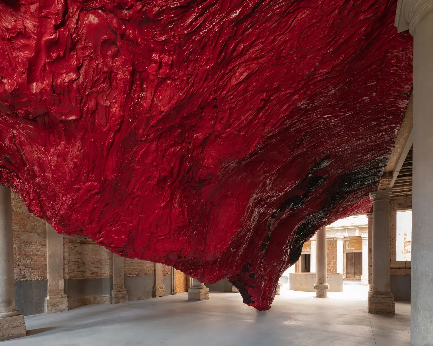 A vast, red, inflated PVC membrane installation filling a large gallery space, with visitors navigating its perimeter.