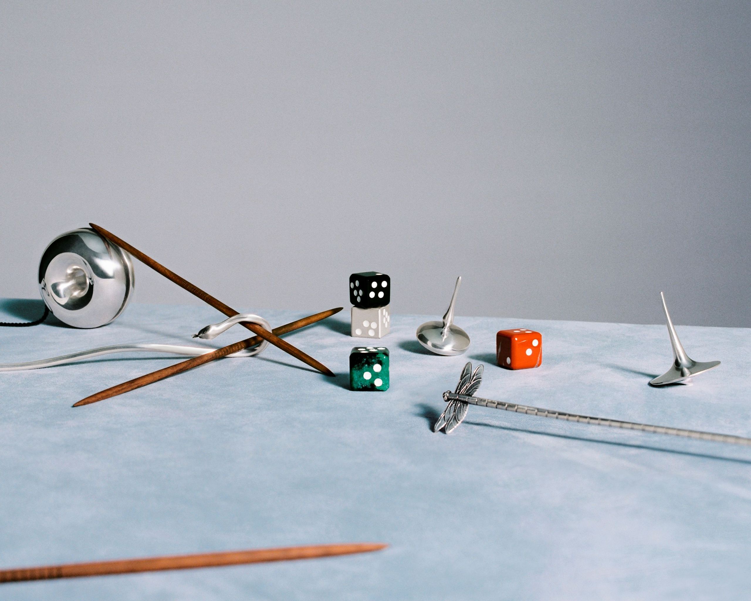 A collection of Georg Jensen silver and stone dice and a Mikado game set displayed on a wooden surface.