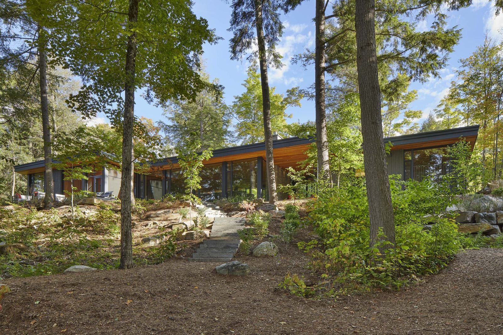 Exterior view of Percy Lake Cottage nestled amongst trees overlooking a calm lake.