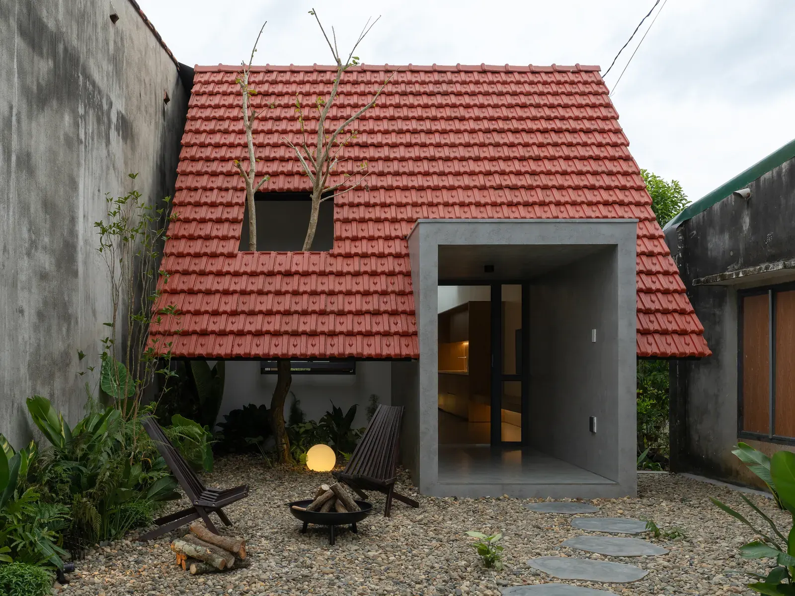 Exterior view of Nam Da House, a minimalist concrete residence in Vietnam, partially screened by existing structures.