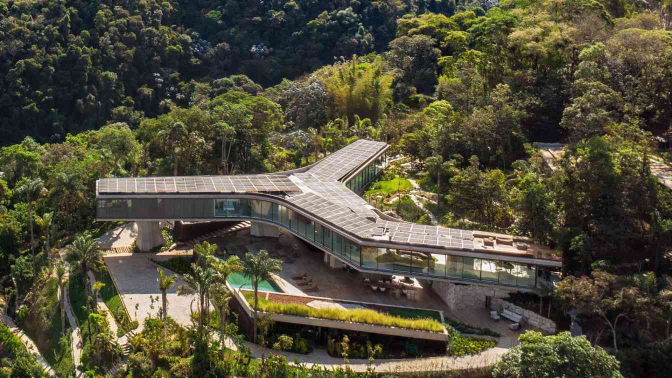 A modern house with cantilevered sections and sculptural concrete pillars nestled into a wooded hillside.