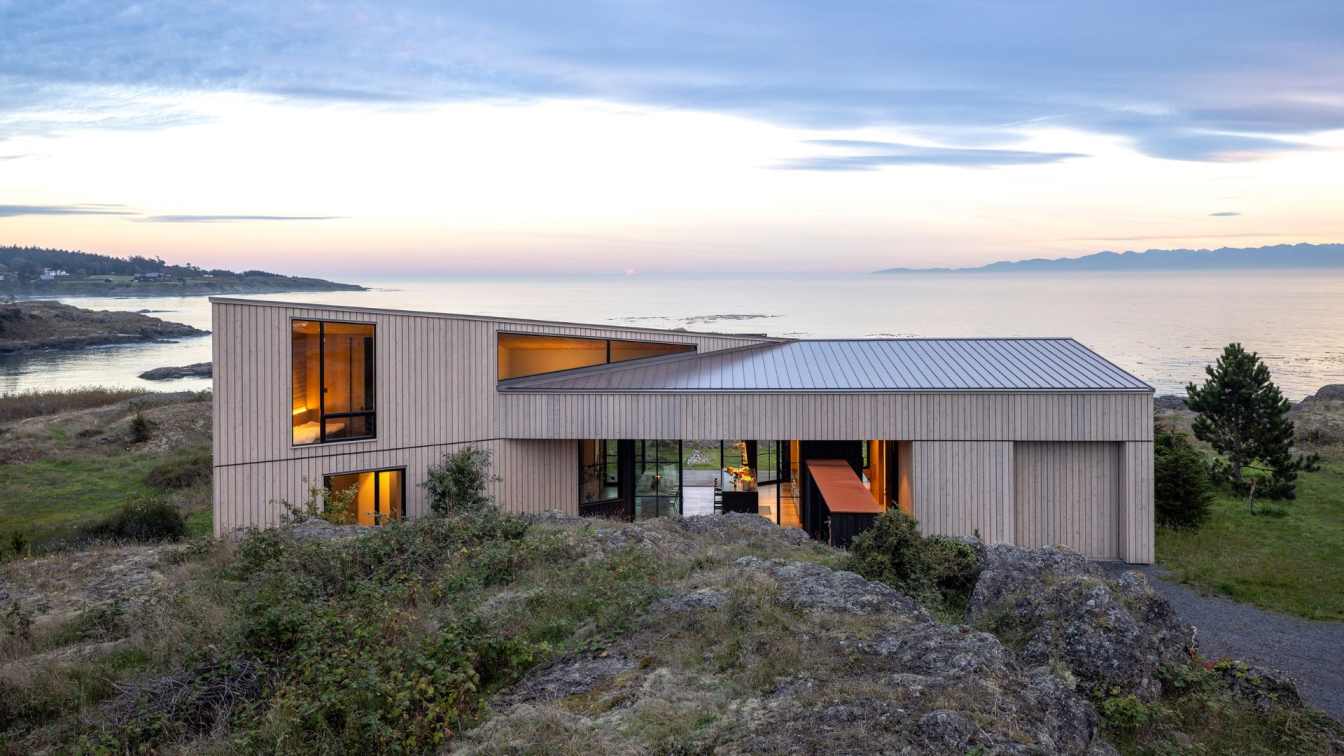 Exterior view of the False Bay Residence on San Juan Island, showcasing its cedar cladding and integration with the rocky shoreline.