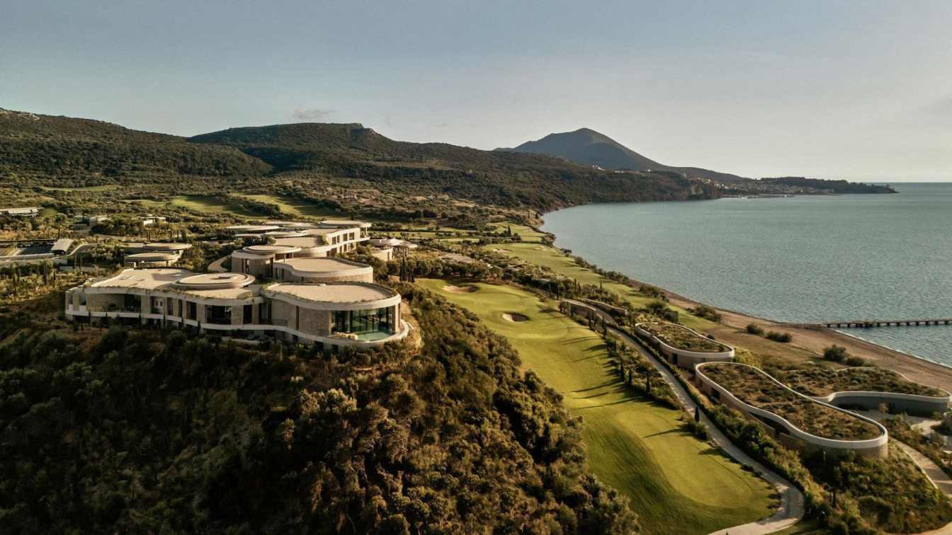 Exterior view of the Mandarin Oriental, Costa Navarino resort, showcasing its integration with the surrounding hills and bay.