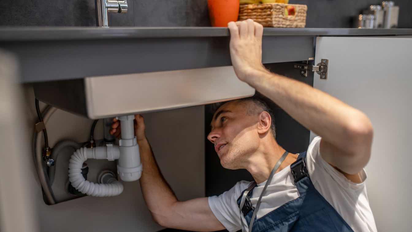 A plumber inspecting a residential plumbing system with tools.