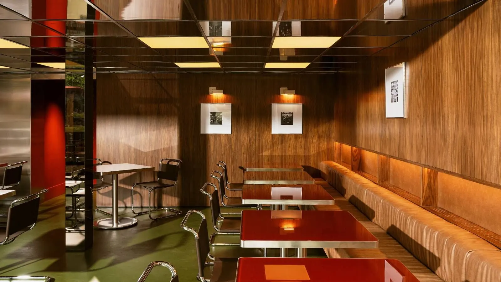 Interior of Lève Office Bar in Turin, featuring a stainless steel counter, deep red backdrop, and reflective surfaces.