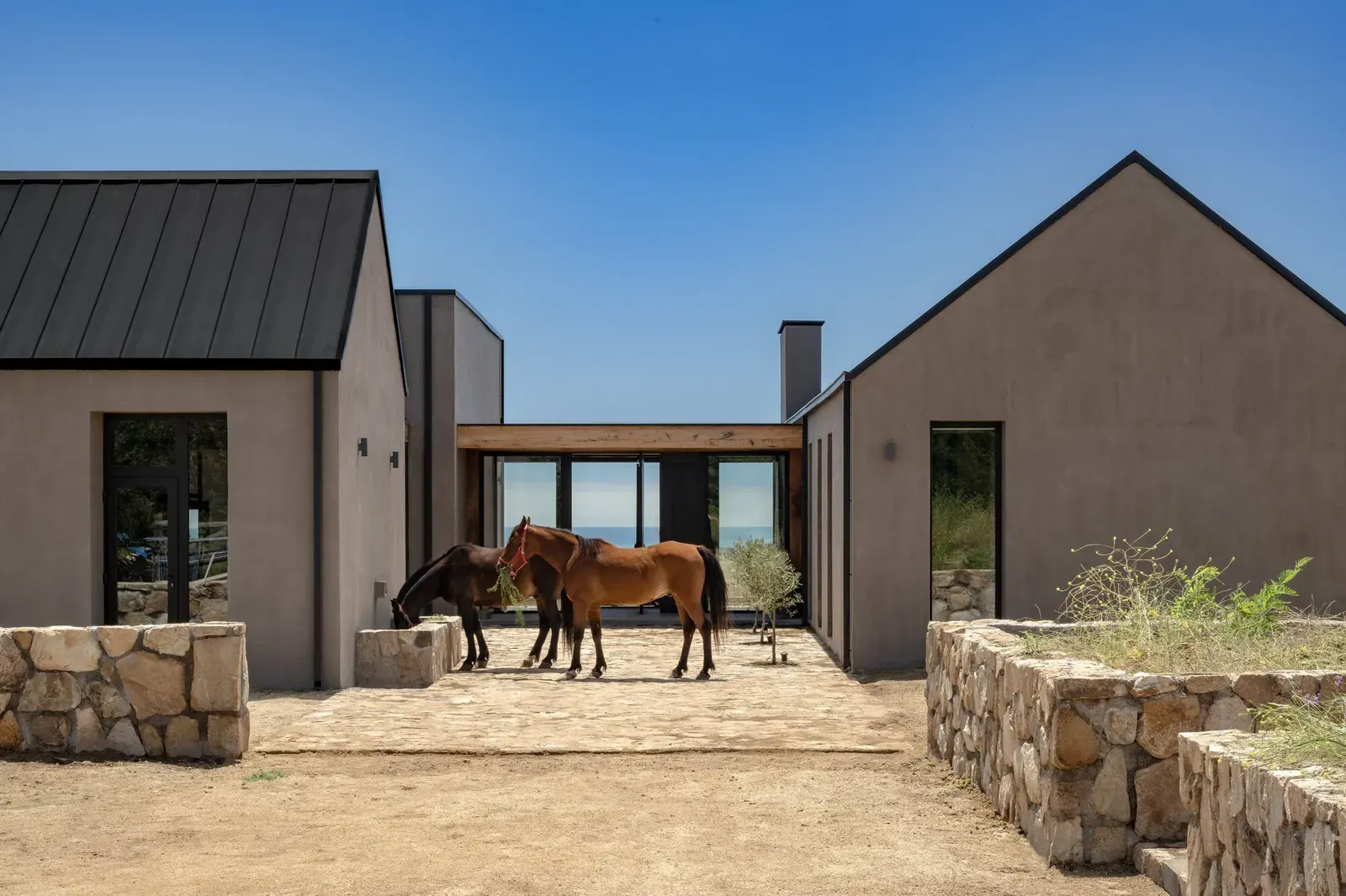 Exterior view of Illapangui del Peumo House by Vergara Arquitectos, showcasing its open courtyard street and distant ocean views.