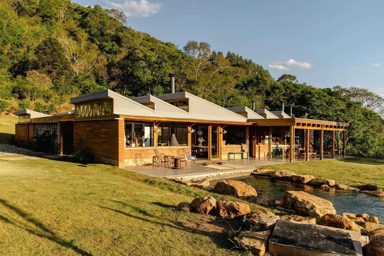 Exterior view of the Matita-Perê House, a contemporary structure nestled within a lush, mountainous landscape.