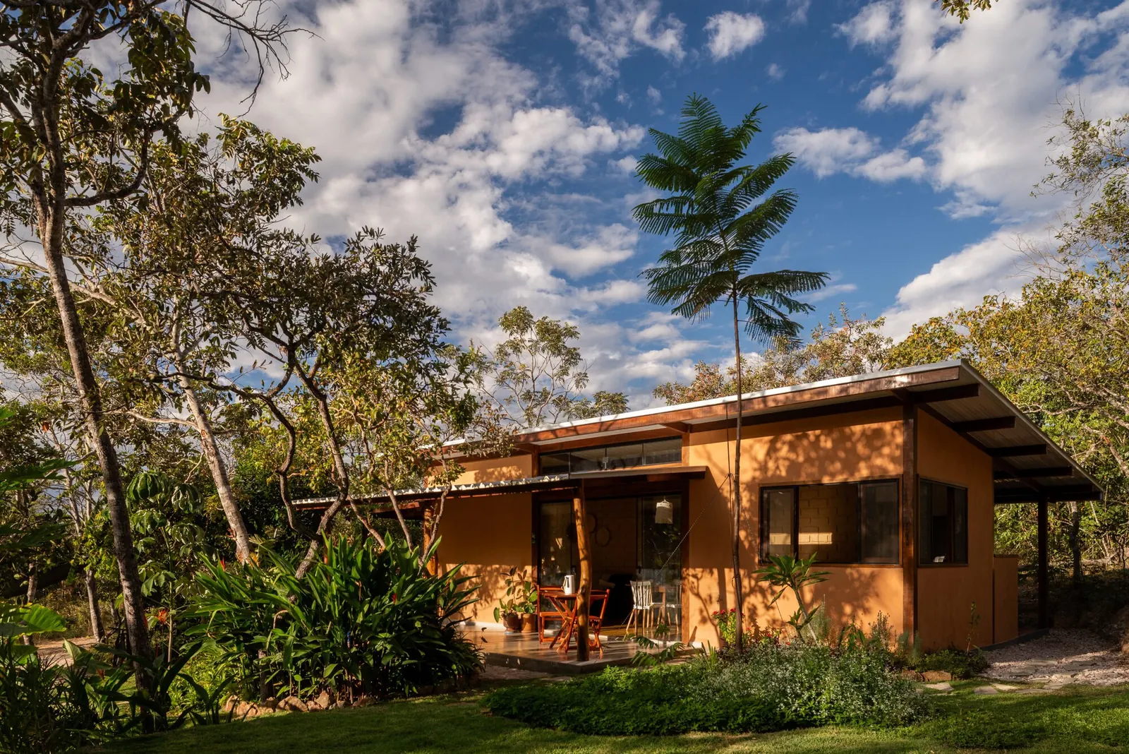 Exterior view of Mel House by Francisco Lang Arquitetura, showing a wooden deck and glass facade against the Cerrado savanna
