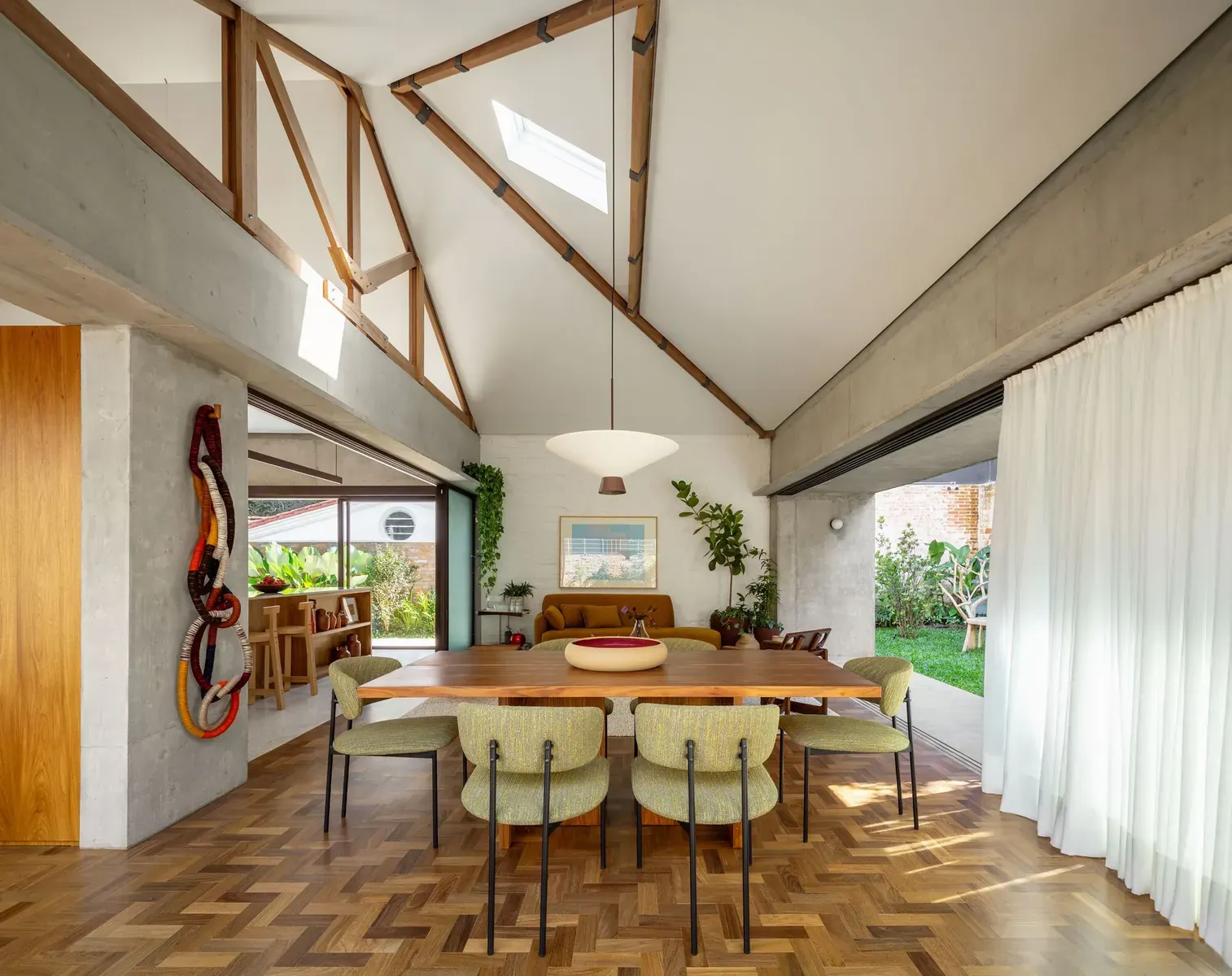 A sunlit living room in the renovated Cafelândia House, featuring large windows overlooking a vibrant garden.
