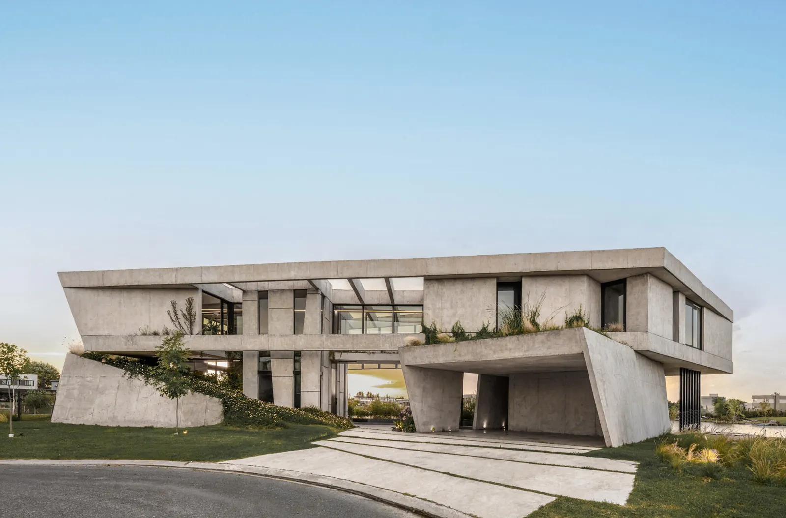 Lomadas House by Grizzo Studio, exposed concrete folded bar on two native‑vegetation mounds, lagoon shoreline, Pilar, Argentina
