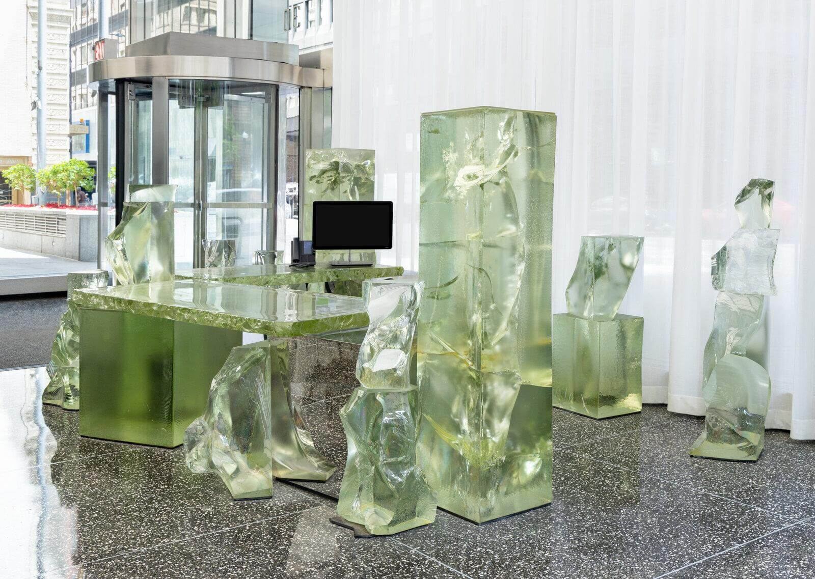 The monolithic "Icehenge Desk" designed by Frank Gehry, constructed from multiple reconfigurable blocks of emerald glass, is presented as sculptural office furniture.