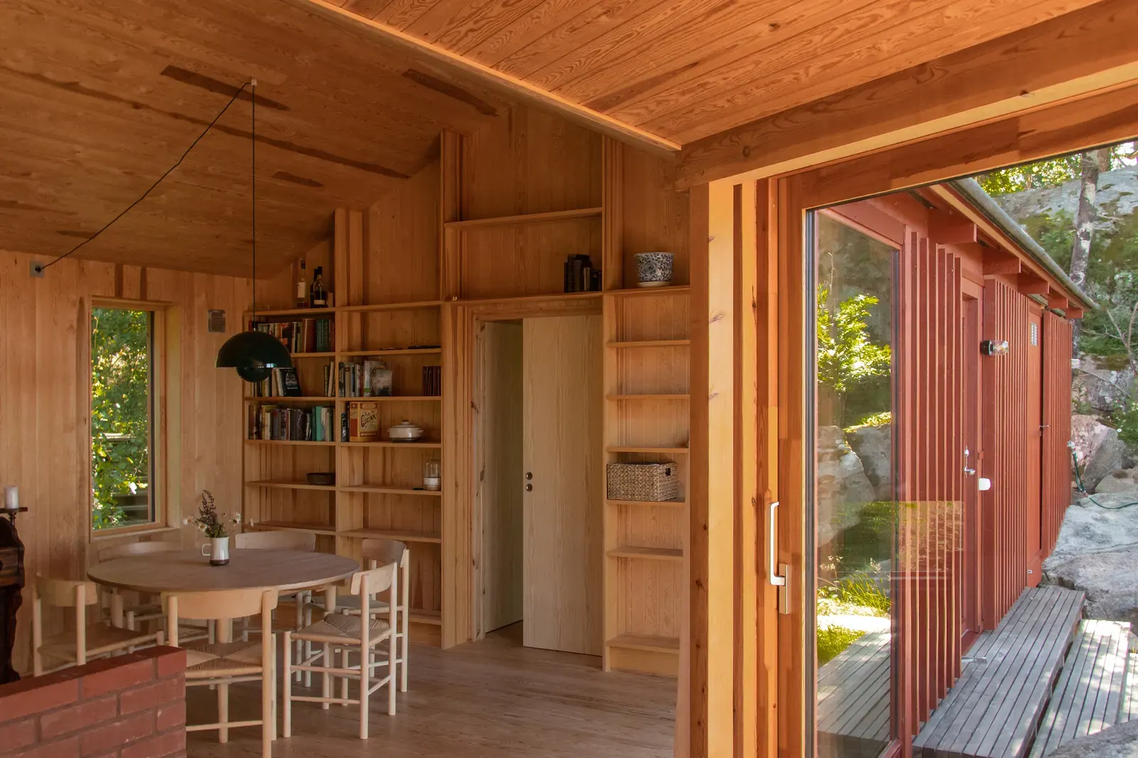 Exterior view of Cabin Åkvåg, a modern wooden cabin nestled in a hilly, tree-covered landscape.