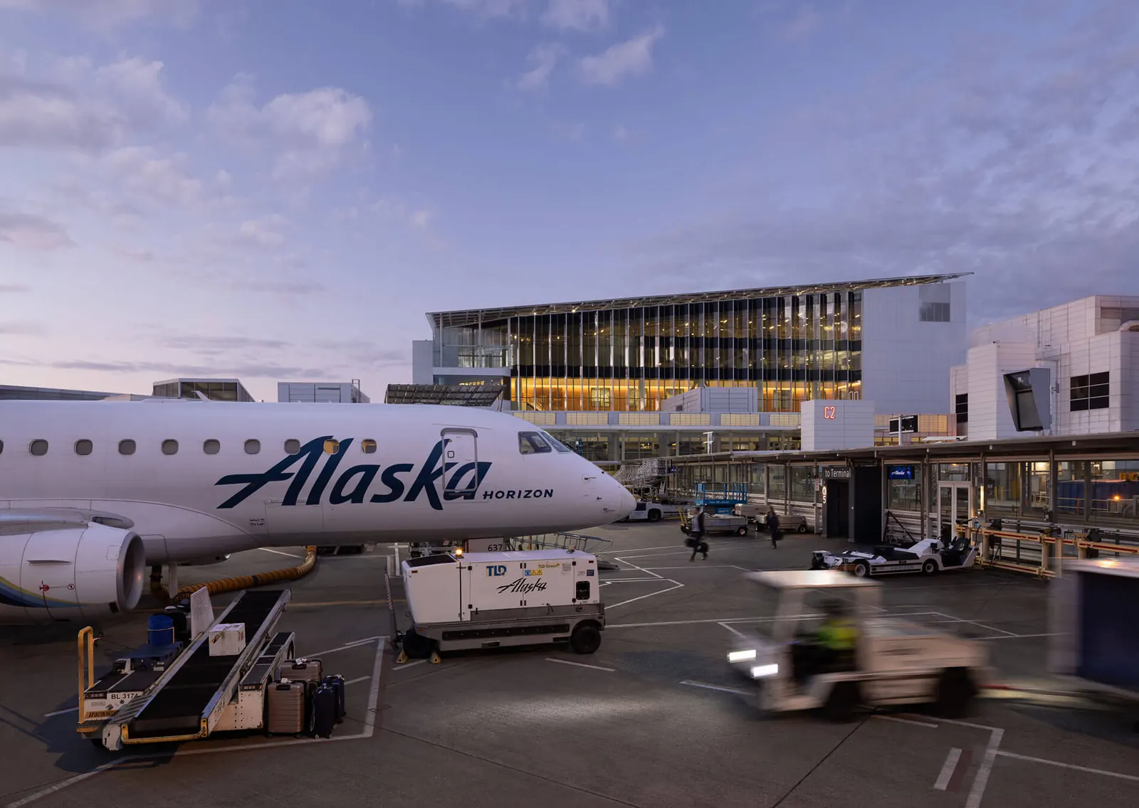 Interior view of the new concourse expansion at Seattle-Tacoma International Airport, featuring a grand staircase, a wooden sculptural element, and natural light filtering through