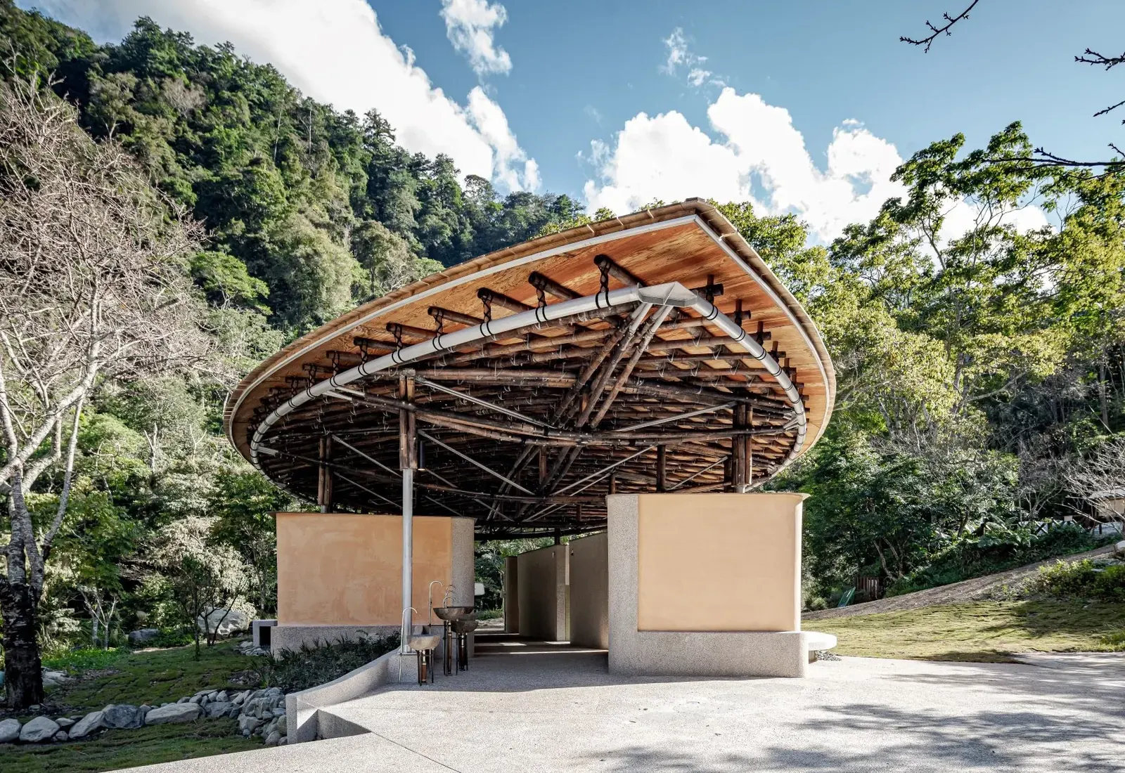 Exterior view of a Basianshan Natural Public Toilet constructed with bamboo, nestled within a forest landscape.