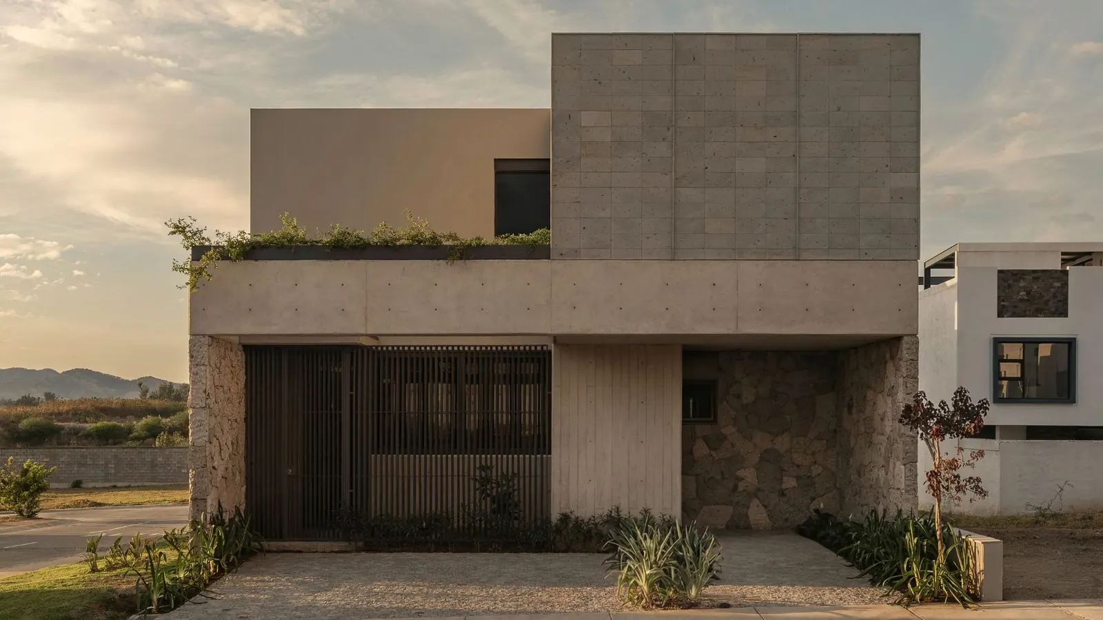 Exterior view of Casa Contreras in Zapopan, showing the solid blind west facade that blocks afternoon solar radiation, with exposed concrete and Cantera stone walls.