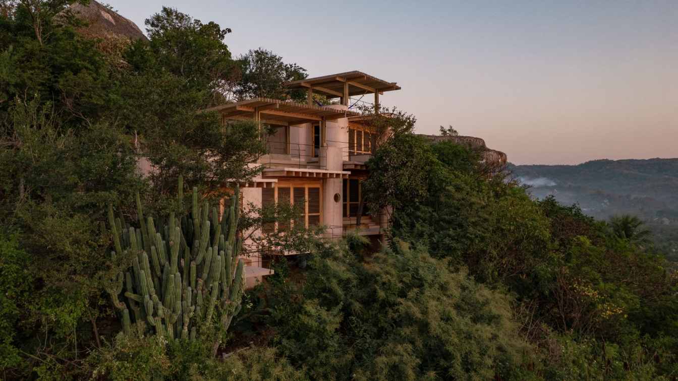 Casa Diez Pies perched on a steep rocky slope above Rinconcito Beach in Mazunte, Oaxaca, with concrete columns lifting the structure above the terrain
