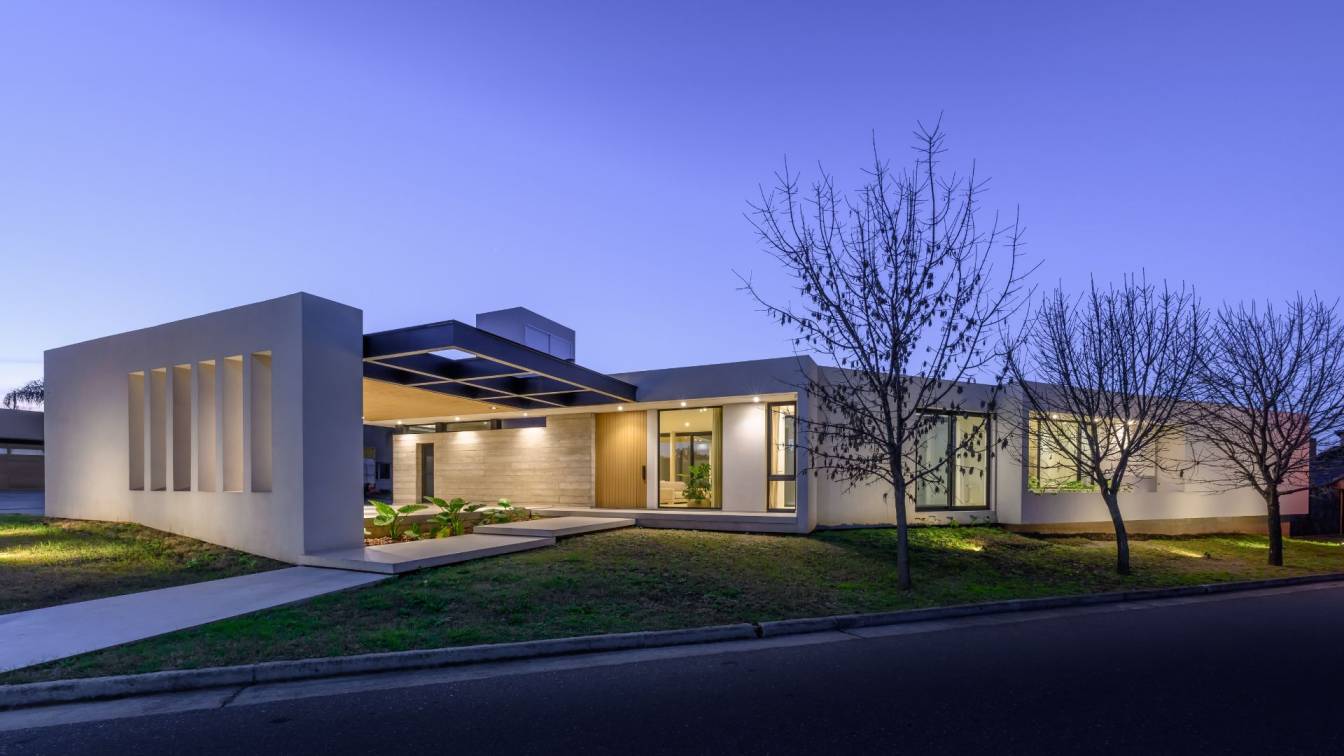 Exterior view of Casa LC, showcasing its perforated concrete wall with sunshades and a prominent cantilevered steel entrance structure.