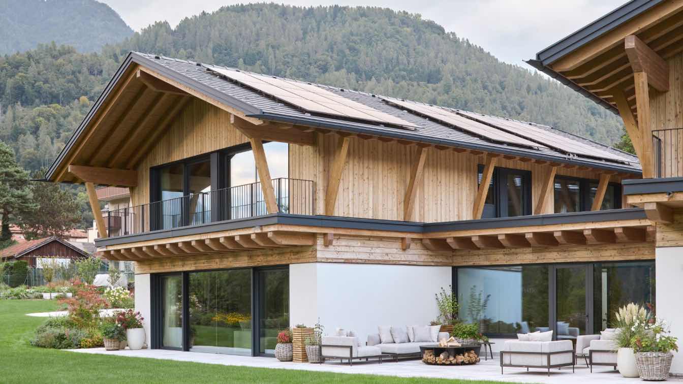 Chalet Sara, a modern mountain residence with timber and stone elements, nestled against a green slope with mountains in the background.