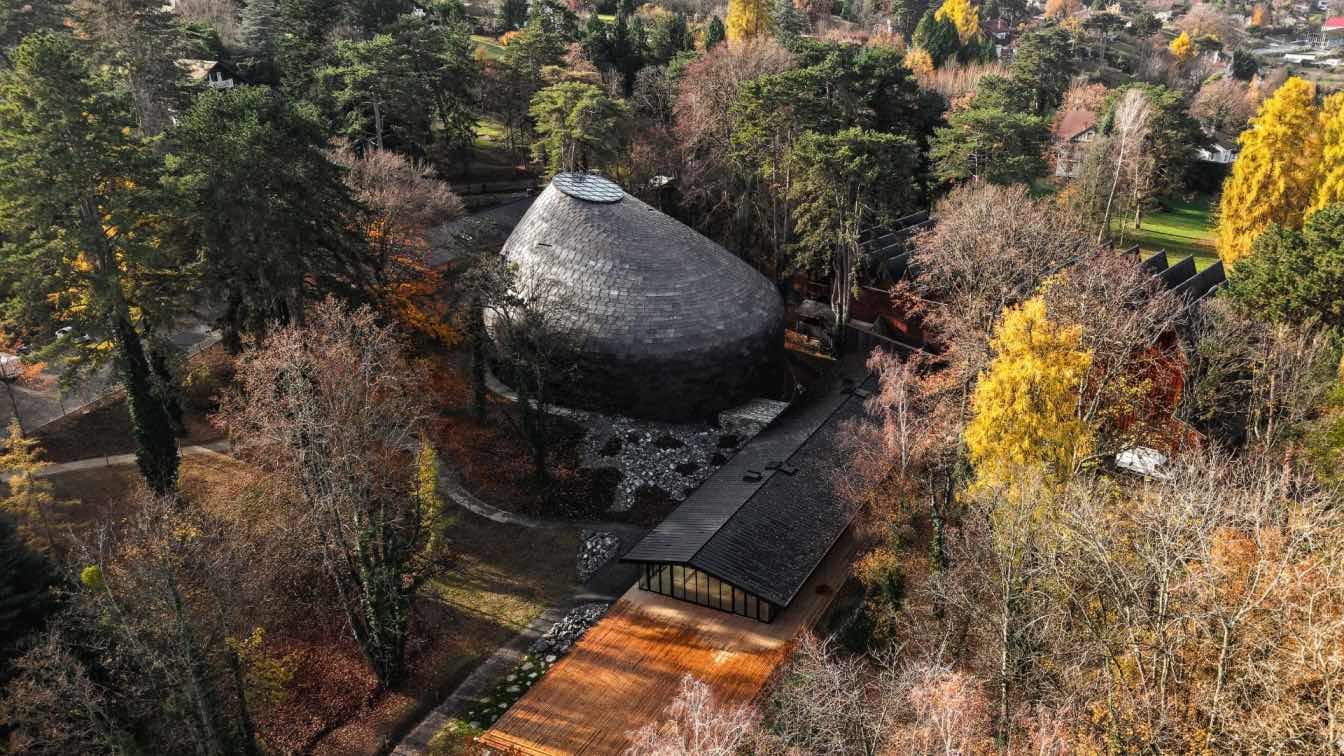 Exterior view of La Source Vive, a contemporary chamber music hall with a copper roof, situated within a lush forest setting.