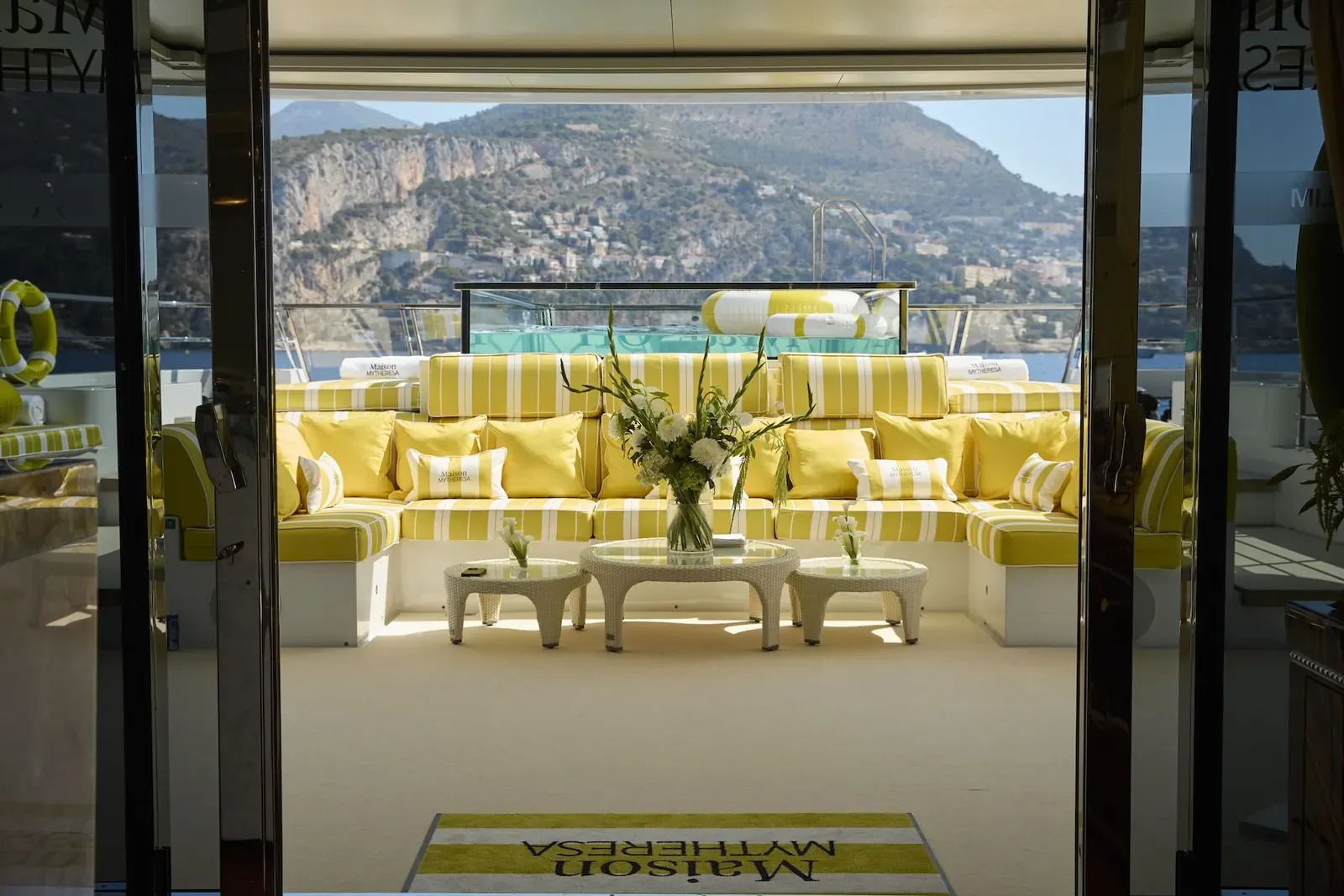 A mega-yacht branded with Mytheresa's signature yellow is seen docked in a picturesque harbour on the French Riviera.