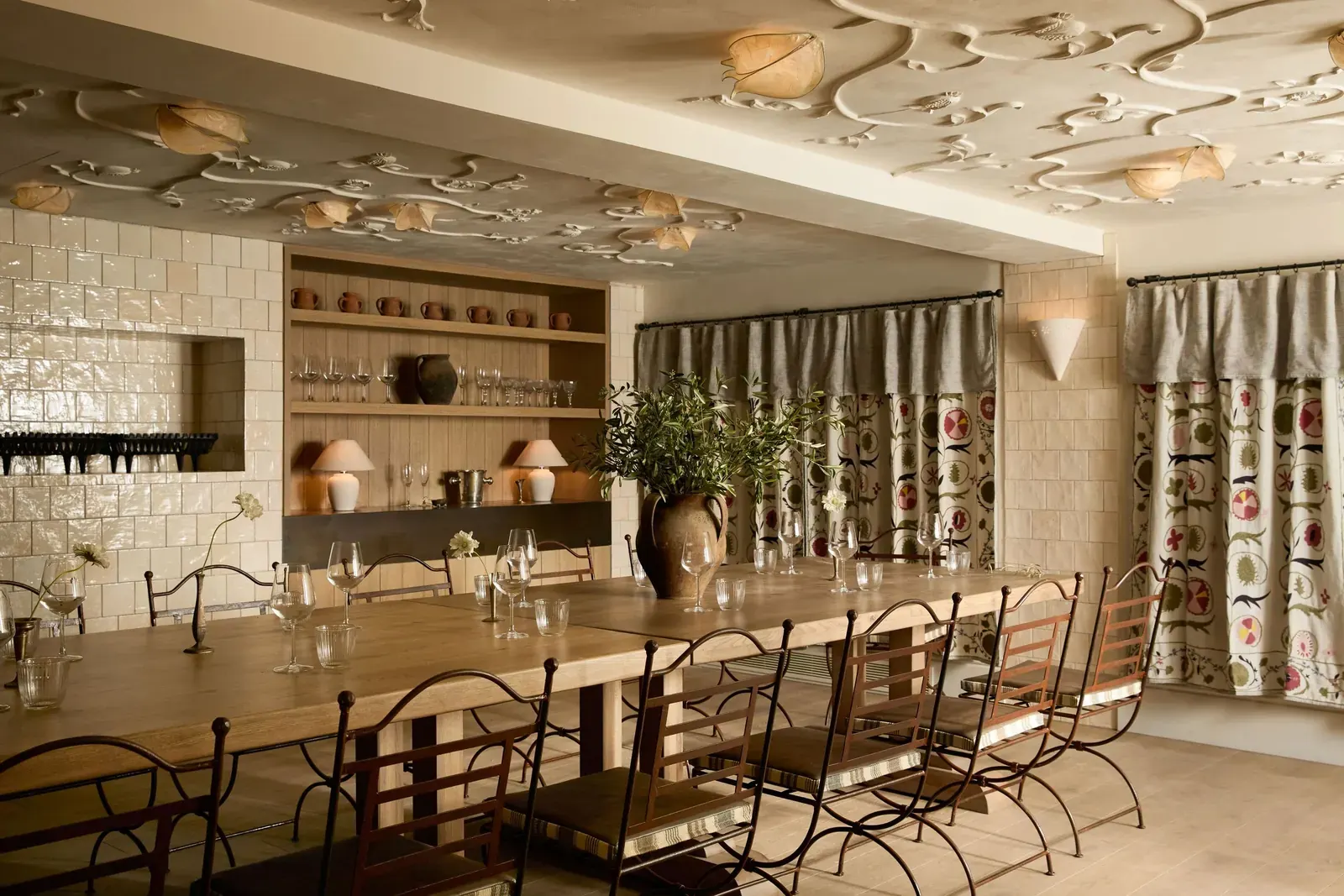 Interior of Kinz restaurant, a Lebanese brasserie in London, featuring bright teal walls, exposed brick, a glowing ochre bar, and a large wine-red lantern overhead.