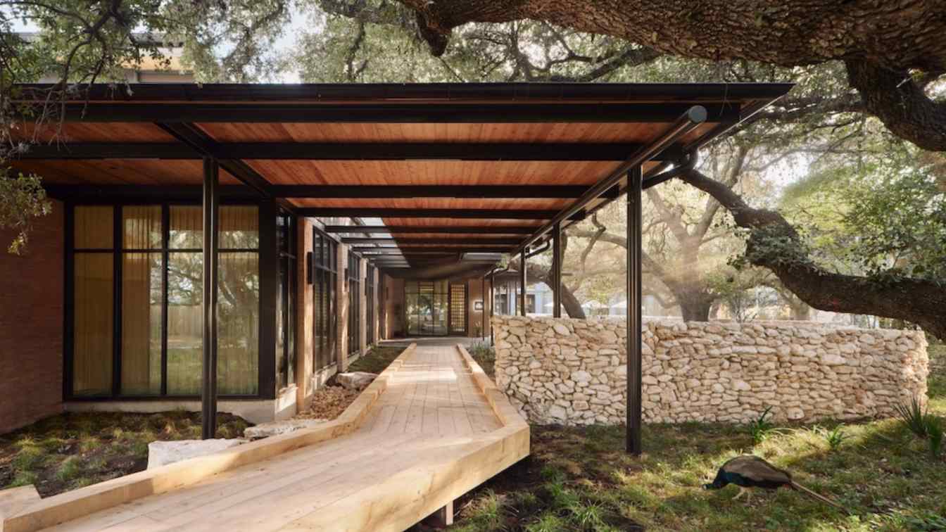 Exterior view of The Inn at Green Pastures, a three-story L-shaped boutique hotel nestled among large oak trees, with a pool courtyard visible.