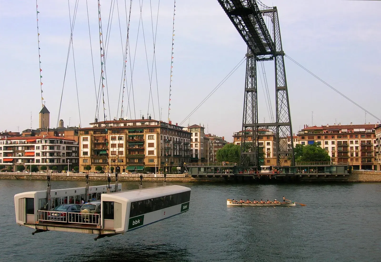 The Bizkaia Bridge, a large iron structure with a suspended gondola, crosses a wide river.