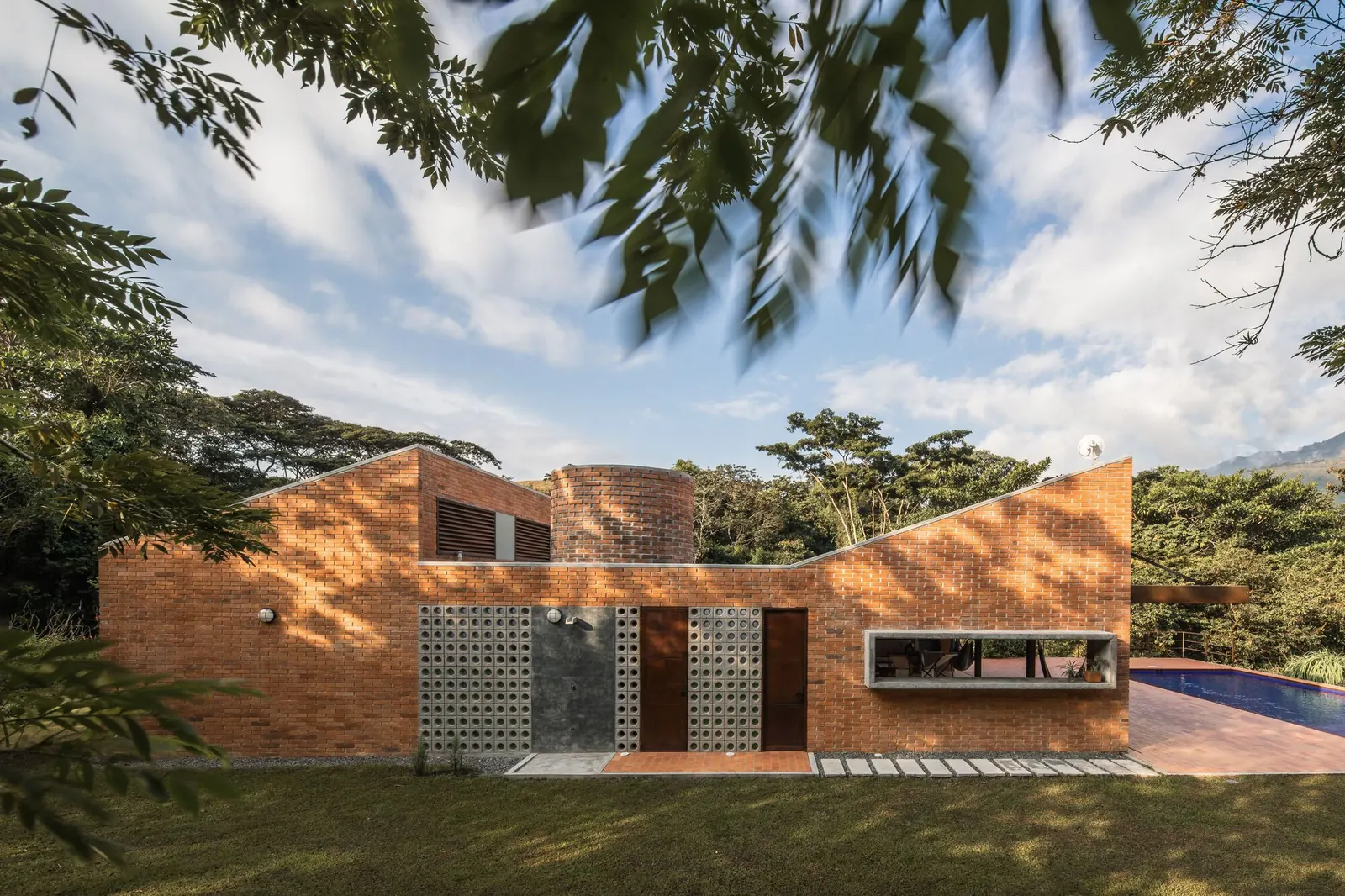 Exterior view of a contemporary Colombian residence featuring textured exposed brick walls and large glass openings