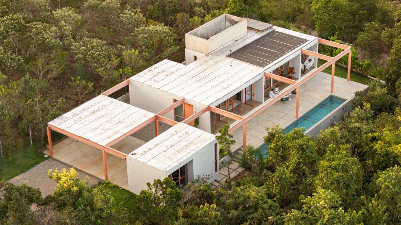 Grota House in Brasília by Esquadra Arquitetos, a single-level residence with orange steel columns and window frames set against dense tropical vegetation