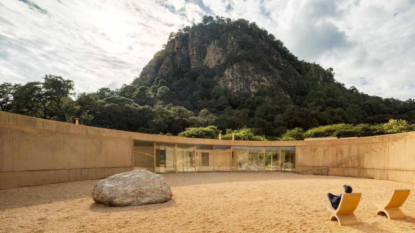 Low circular house with earth-colored concrete walls blending into the forest and prairie landscape of La Reserva Peñitas, Mexico