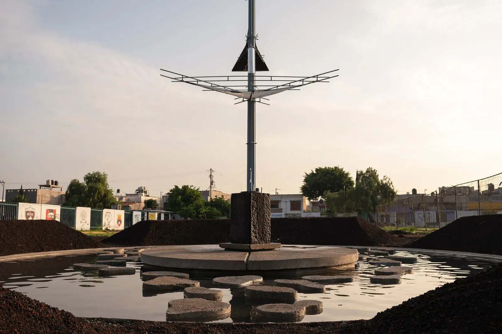 Rain Rhizome installation by TANAT and Rizoma del Agua in Chimalhuacán, Mexico, with a wooden canopy and central water container in a public space.