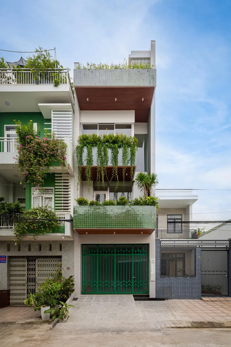 Calm Haven House, a residential project by ADA Design & Build in Can Tho, Vietnam, showcasing a modern concrete facade with brick and stone accents, surrounded by greenery.
